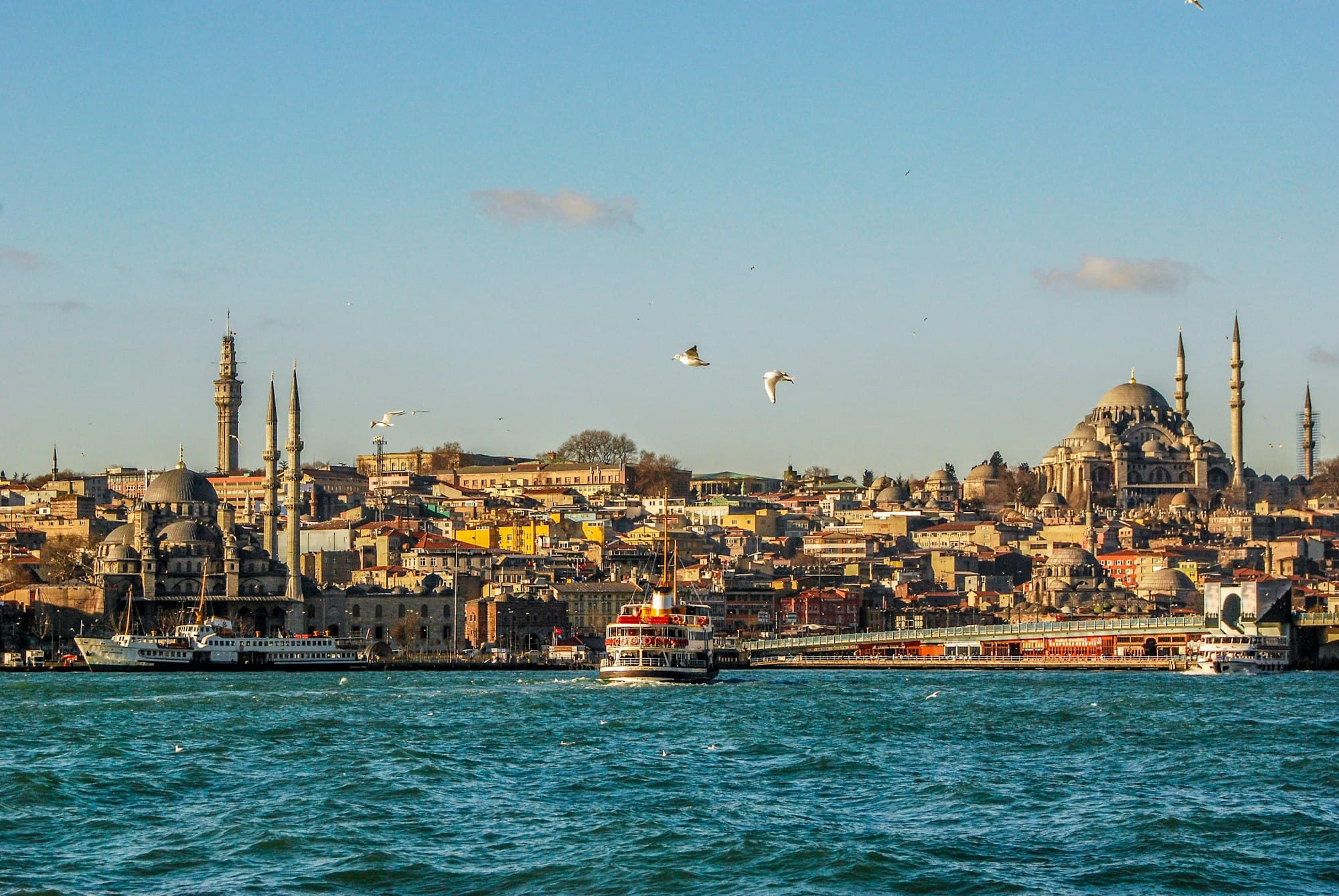 A ferry crossing the Golden Horn in late sun, with the Eminönü skyline, the New Mosque and the Süleymaniye behind it
