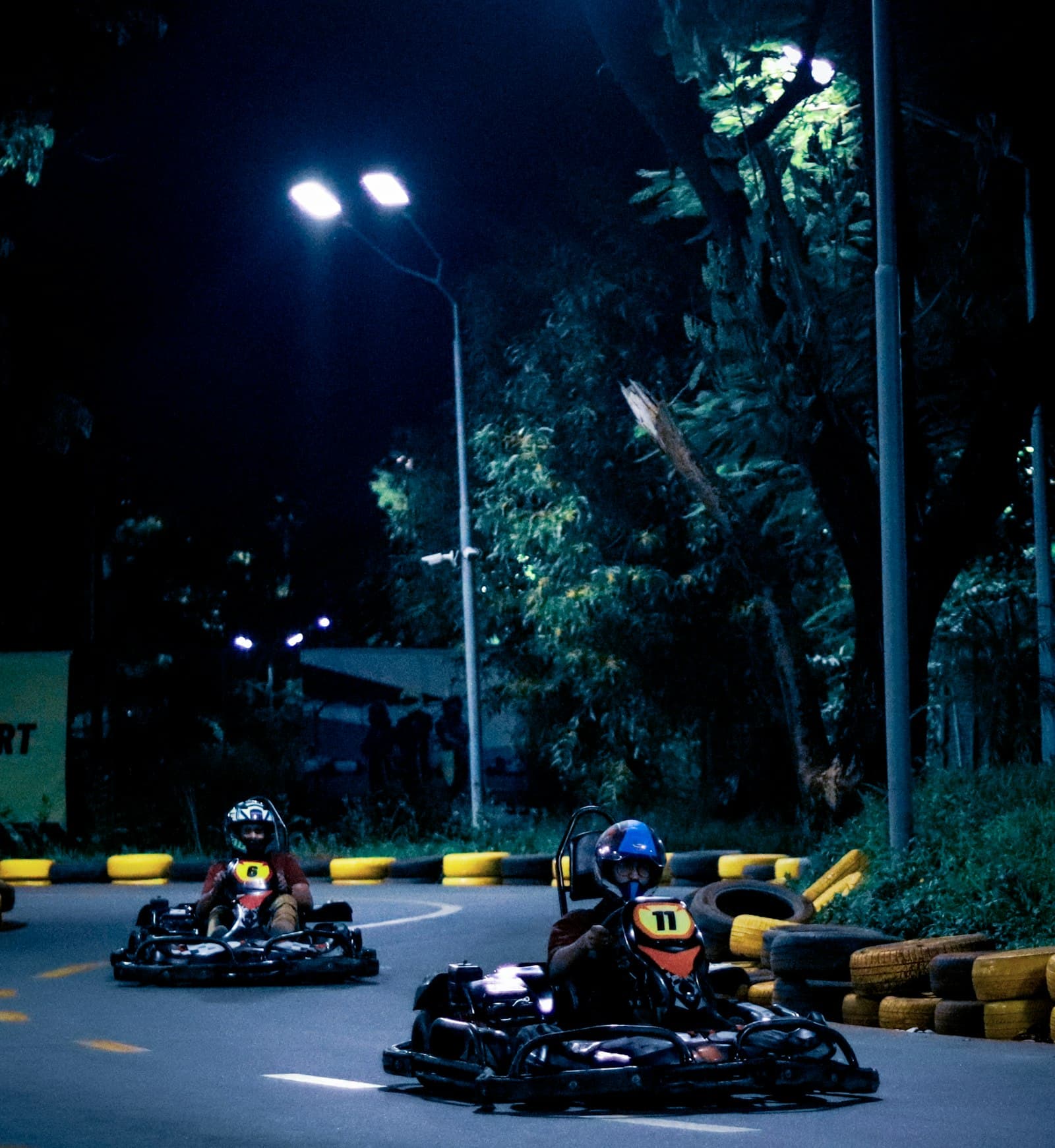 Go-karts racing on a lit night track with helmets and tire barriers