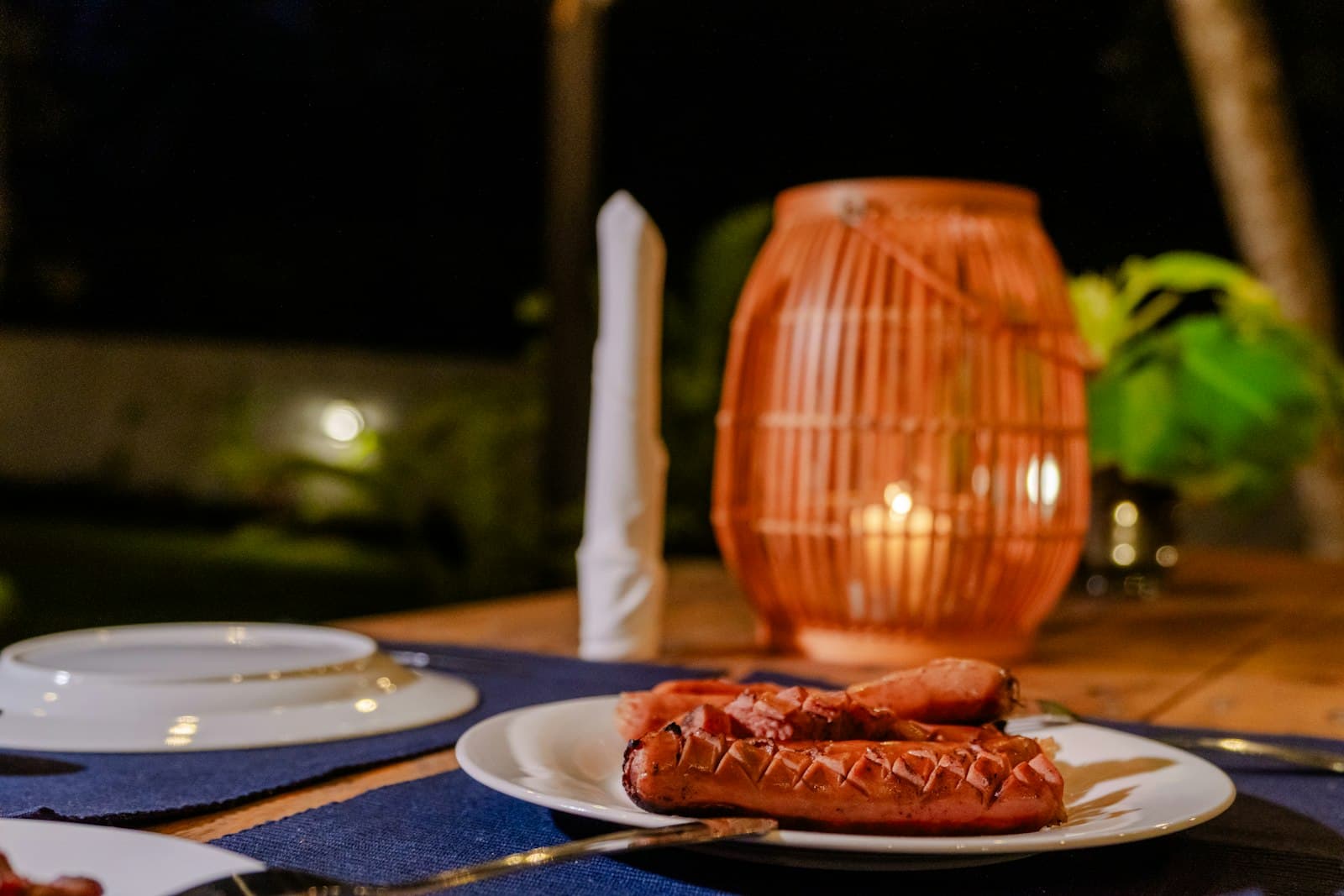 Outdoor villa BBQ at night: grilled meats, lantern, candlelit table