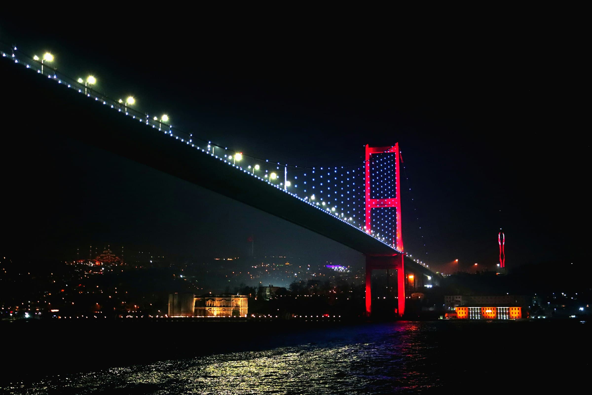 The 15 Temmuz Şehitler Bridge over the Bosphorus at night, illuminated against a black sky with the lights of Istanbul behind