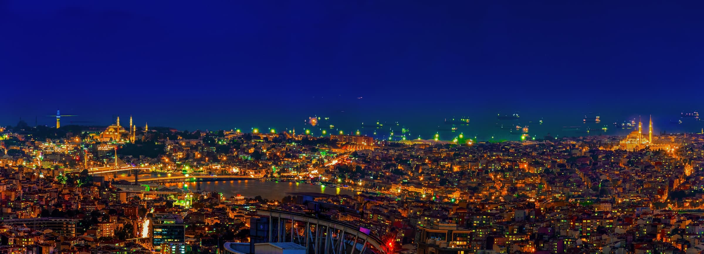 Wide aerial panorama of Istanbul at night with mosque silhouettes flanking the city lights
